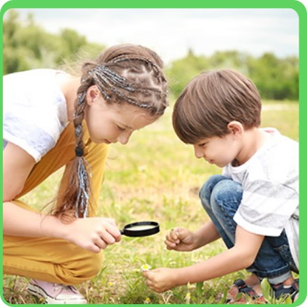 Dwoje dzieci badające przez lupę jakiś okaz na łące - Akademia Lesna